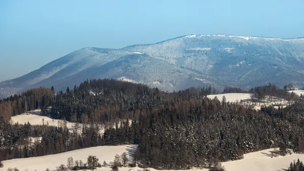 Zasněžený beskydský vrchol nad lesy a loukami